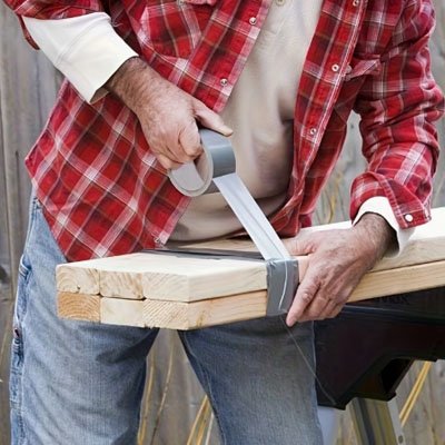 Homme avec chemise carreaux rouge relie six planches avec rouleau Ruban adhesif gris resistant