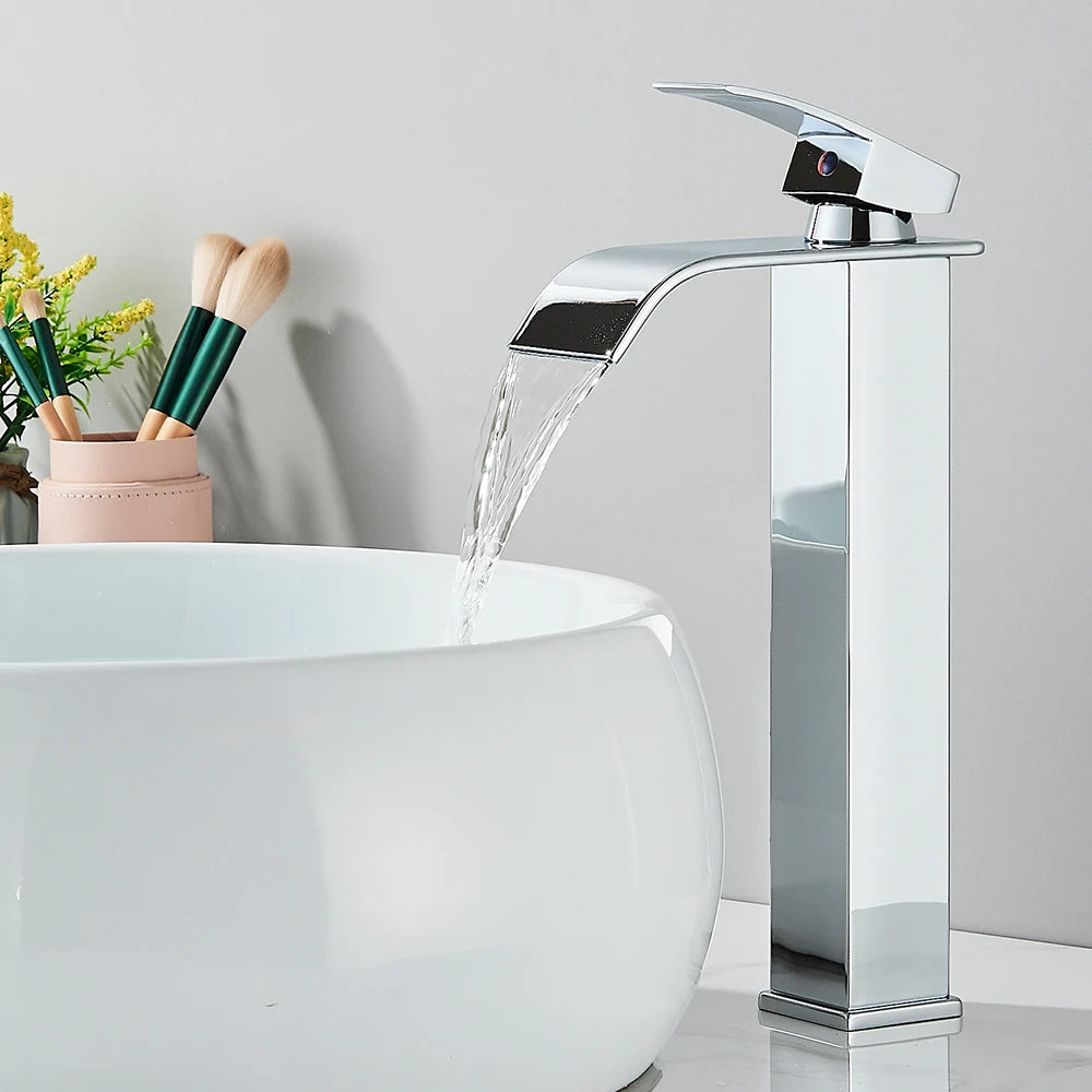 Robinet salle de bain argente long, eau limpide coule cascade, lavabo blanc sphérique, pinceaux maquillage et fleurs jaunes dans un pot rose