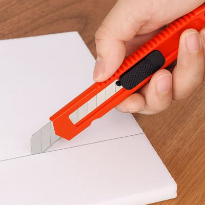 Cutter orange tenu par main qui coupe blanc