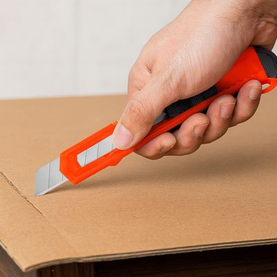 Cutter orange tenu par main qui coupe emballage en carton