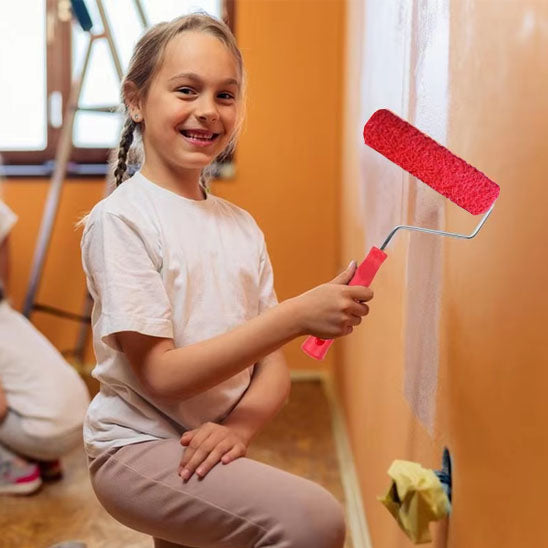 Fillette souriante tient rouleau peinture rouge avec poignée rouge, mur orange