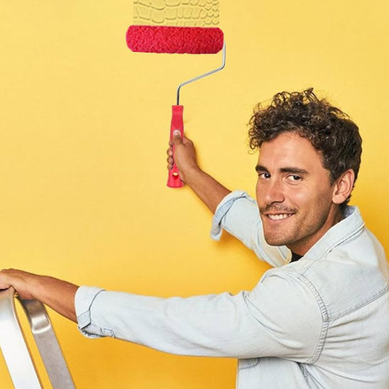Homme souriant tient rouleau peinture rouge avec poignée rouge, mur jaune
