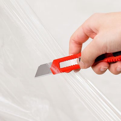 Cutter orange tenu par main qui coupe cellophane