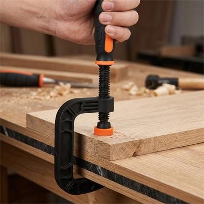 Menuisier utilisant un serre joint en C rapide pour assemblage et serrer des planches de bois sur un établi d'atelier