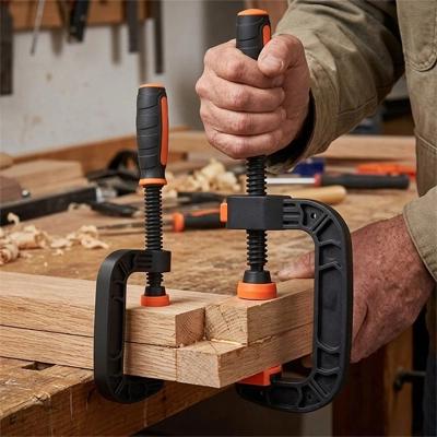 Menuisier utilisant un serre joint en C rapide pour assembler et serrer des planches de bois sur un établi d'atelier