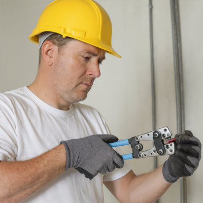 homme  avec casque jaune et gants noirs  tenant pince a sertir bleue avec cosse 