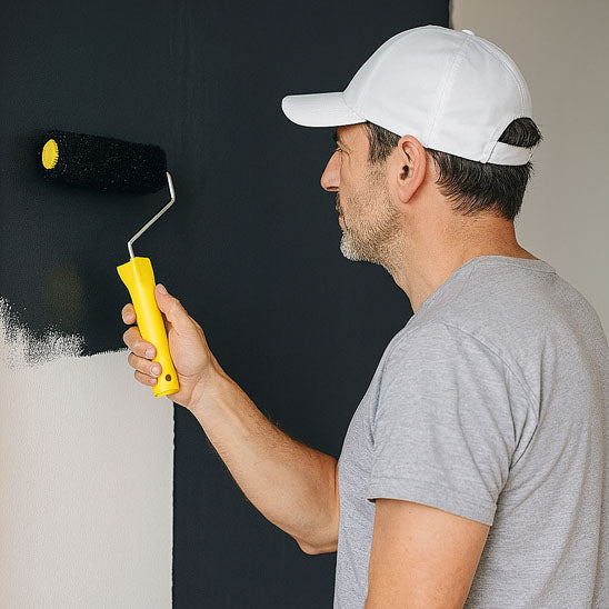 homme avec casquette blanche pull gris peint mur en noir avec Rouleau peinture