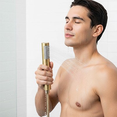 homme tient Pommeau de douche dore sous  douche