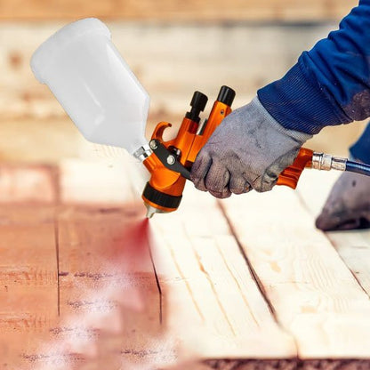 main avec gants blancs , manches bleues tient Pistolet peinture orange godet blanc une planche en bois