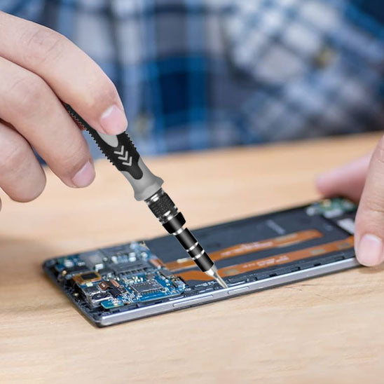 main d'un homme tient Tournevis 115 en 1  et repare smartphone ouvert
