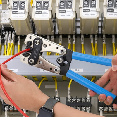 Mains tenant pince a sertir bleue avec cosse gaine à rouge devant tableau électrique
