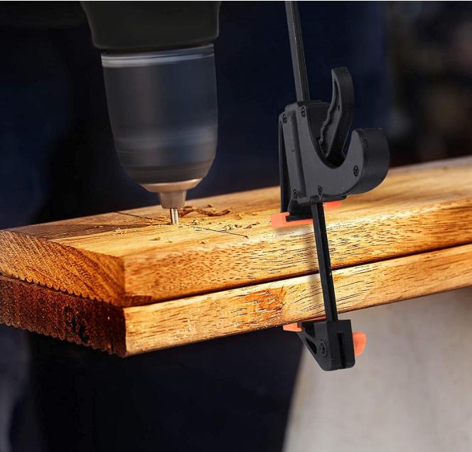 Perçage d'une planche de bois maintenue par un serre-joint à barre en F pendant le perçage