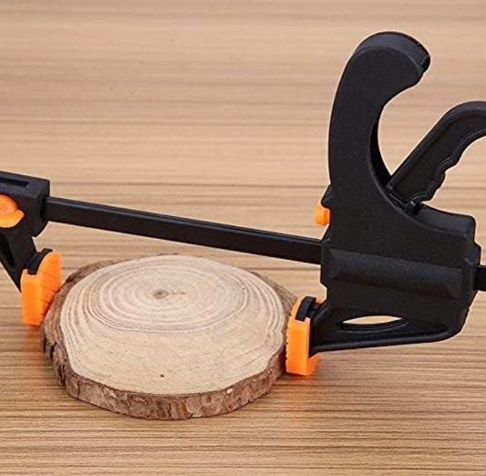 Serre joint à cliquet noir et orange maintenant une rondelle de bois brut sur un établi