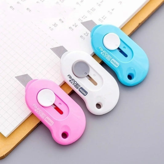 Trois cutters blanc rose et bleu sur papier blanc et plaque de découpe jaune